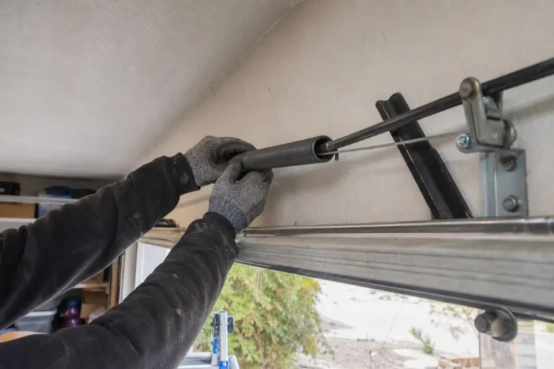 Gloved hands holding a long spring beside an overhead garage-door track